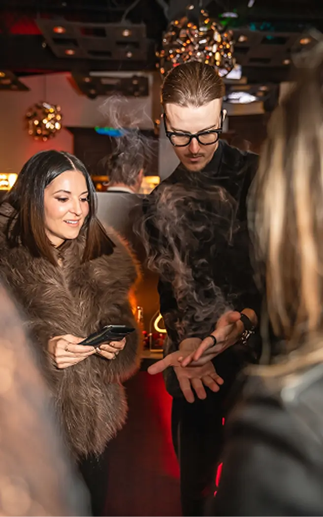 Roman showing a trick to a guest in a fur coat under golden lights
