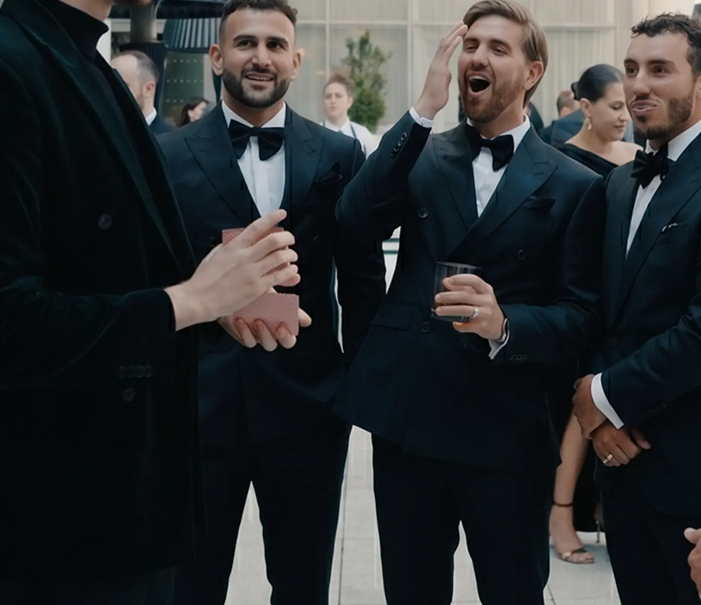 Guests in tuxedos reacting to a trick with laughter and disbelief