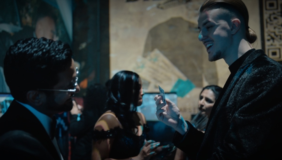 Roman Royss smiling as he shows a playing card to guests
