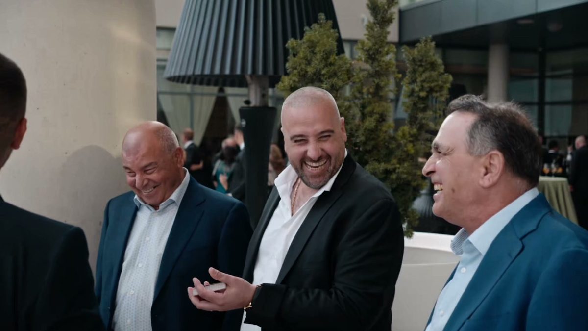 Three guests laughing on a terrace, one holding a deck of cards