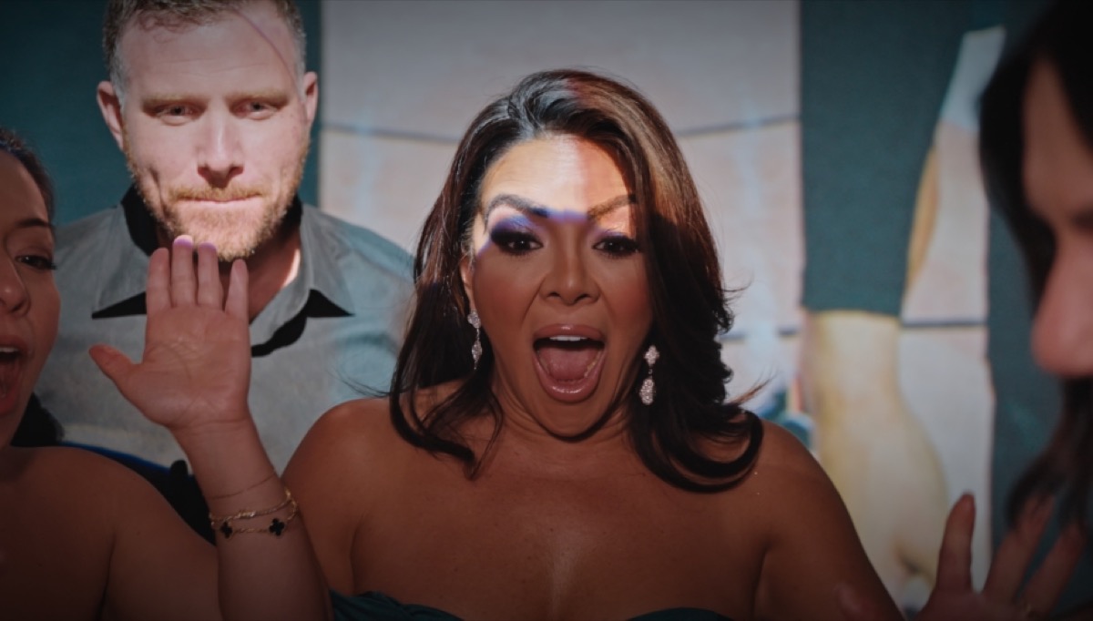 A guest with her mouth open in surprise, a man behind her raising his hand