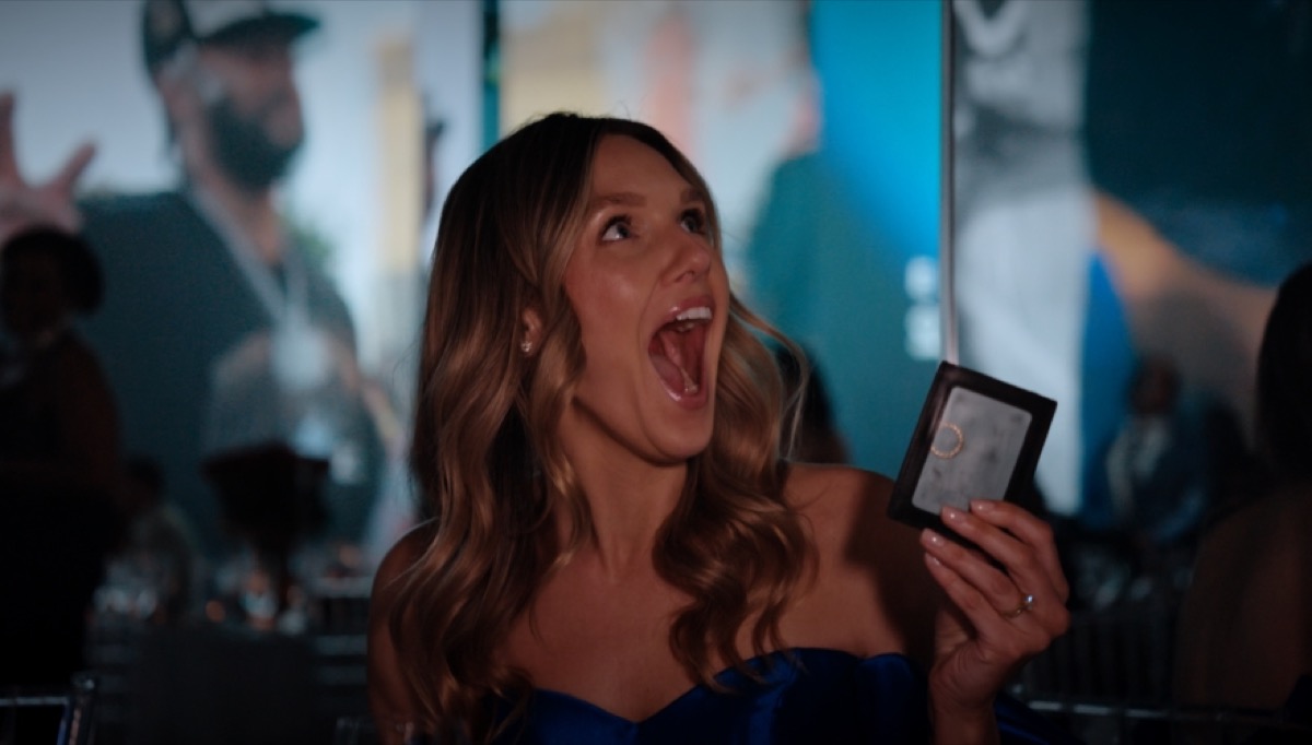 A guest in a blue dress gasping in surprise while holding a small card case