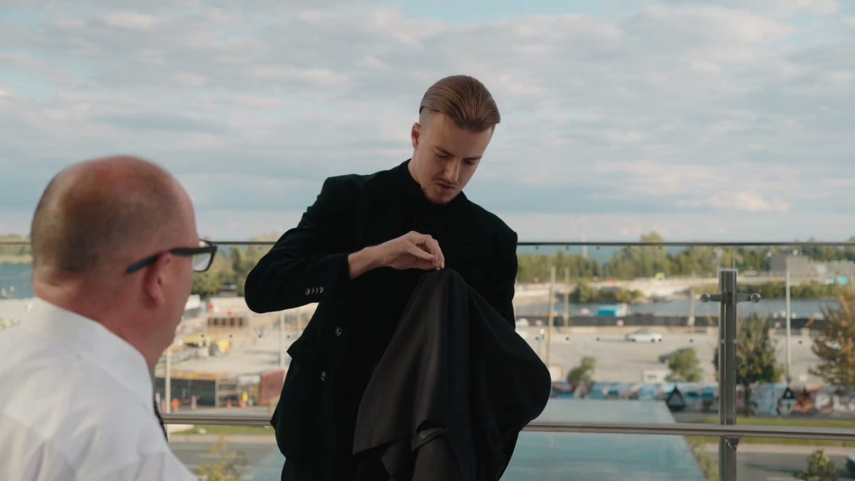 Roman Royss holding a black cloth on a rooftop terrace while a guest in glasses watches