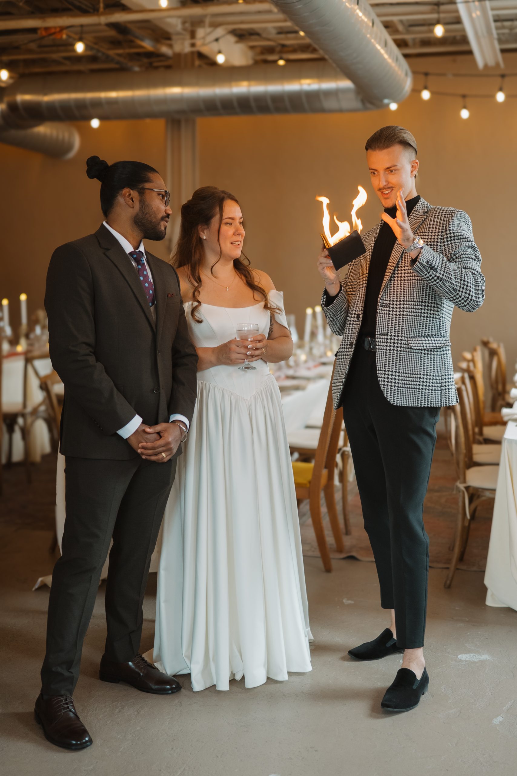 Magician Roman Royss holds up a flame in his hand beside a bride and groom at a wedding reception