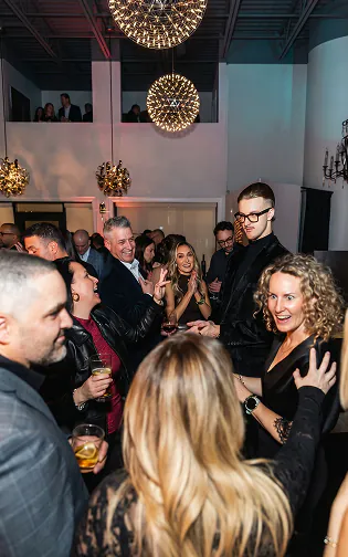 Roman Royss performs close-up magic as smiling guests gather around him at an engagement party